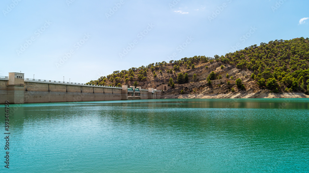 Landscape in which you can see the wall of the Amadorio reservoir in Villajoyosa with the turquoise water and the mountains with wild vegetation that surrounds it (Spain). Sunny summer day.