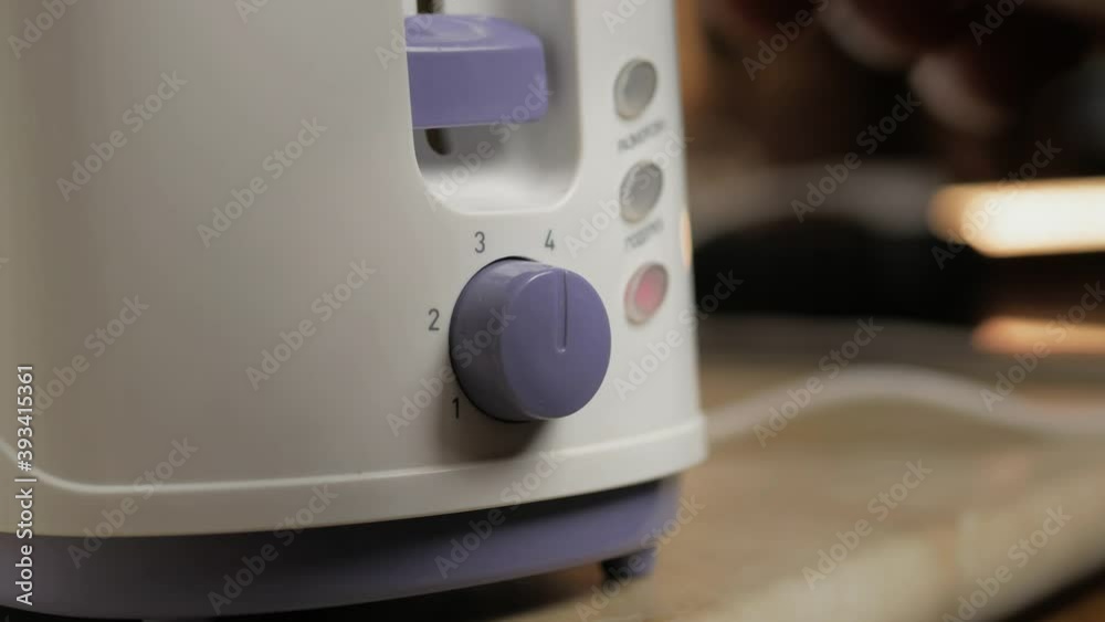 a man's hand sets the temperature of toasting bread on a white toaster a man's hand sets the temperature of toasting bread on a white toaster