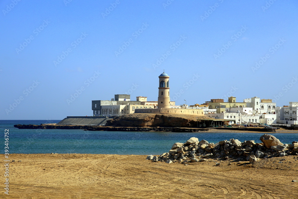 The town of Sur on the sea and the lighthouse of Al Ayjah, at the entrance to the port, both seen from the beach, Oman