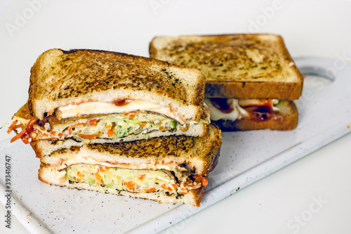 Homemade Korean toast sandwich with eggs, cabbage, carrots, onions, mayonnaise, ketchup and cheese in a cut with visible filling on a white board. DIY fried Korean sandwich, close-up