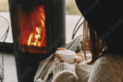 Photography Stylish woman in sweater relaxing with warm cup of tea at modern fireplace with