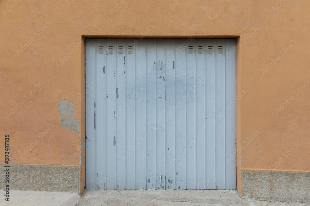 Damaged old blue garage door in the orange wall, shutter closed and blank, space for text