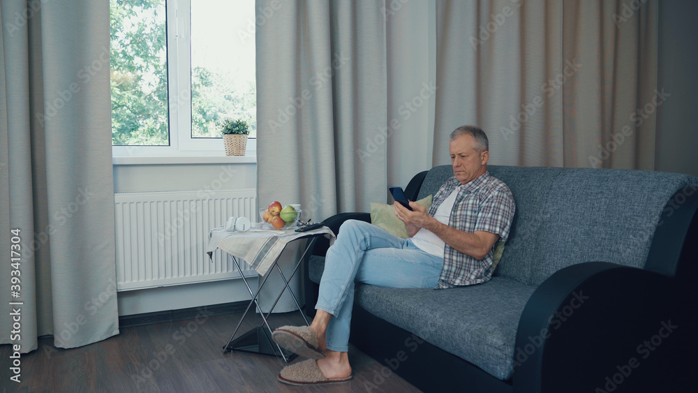 A man reads the news on the phone, sitting on the couch.