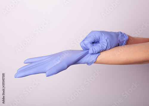 Female doctor putting on blue gloves on white background 