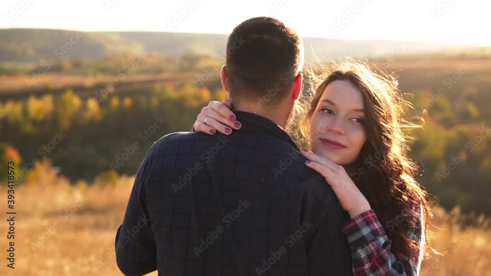 A young couple in love gently cuddles in the middle of the hill against the autumn forest, sunset. A young couple in love gently cuddles in the middle of the hill against the autumn forest, sunset.