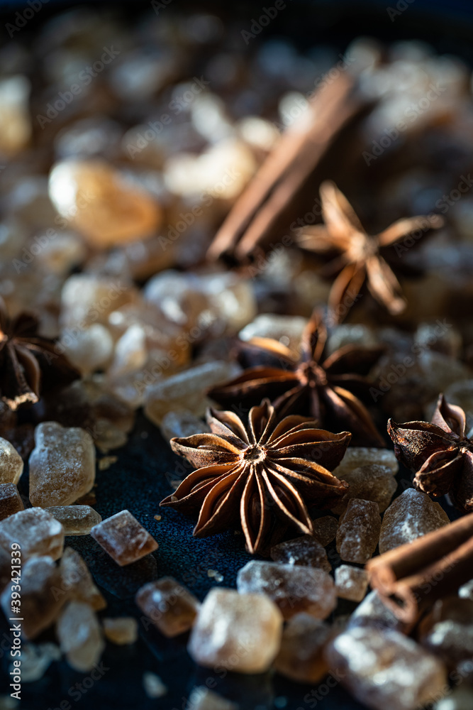 Close up brown sugar crystals, anise stars and cinnamon sticks on deep blue background.
