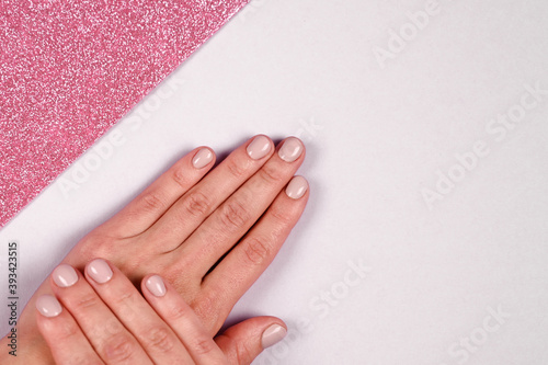  Short nails with pastel color manicure. Empty female hands on white and pink background with copy space. Fashion and beauty concept