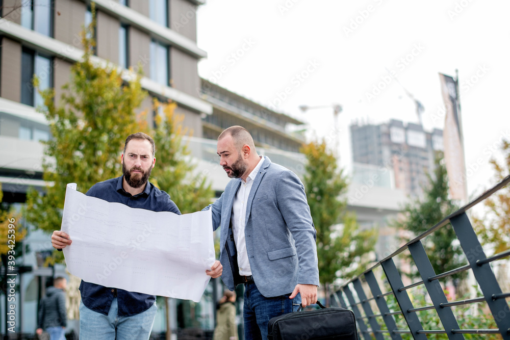 Two young engineers checking the architectural plan outdoors Two young engineers checking the architectural plan outdoors