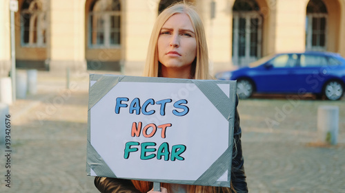 Facts not fear slogan on protest walk. Woman with steamer walking on the street. © art24pro