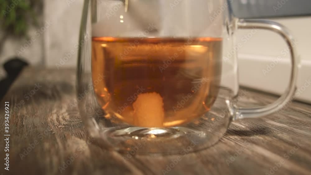 Close up view female hands add sugar cube in fresh-brewed tea, stir spoon sweetener in glass cup. Pleasant ritual in morning. Sugar addiction and intake