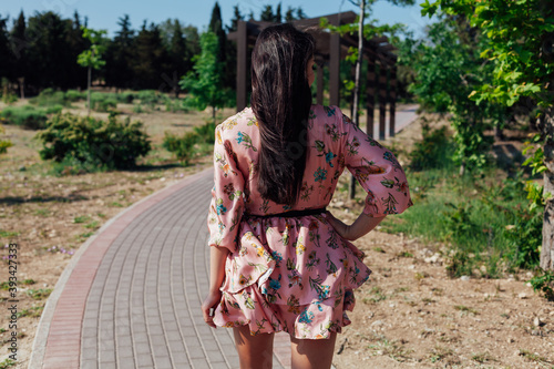 Beautiful brunette woman in a dress with flowers walks in the park alone