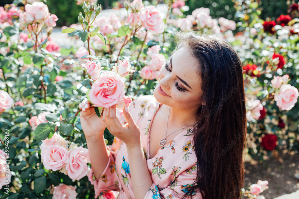 Fototapeta premium Beautiful brunette woman in a dress with flowers with fragrant roses