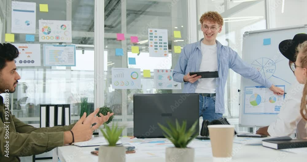 Likable smiling confident skilled man with curly hair holding a presentation for his professional experienced mixed race colleagues and analyzing with them infographics Likable smiling confident skilled man with curly hair holding a presentation for his professional experienced mixed race colleagues and analyzing with them infographics