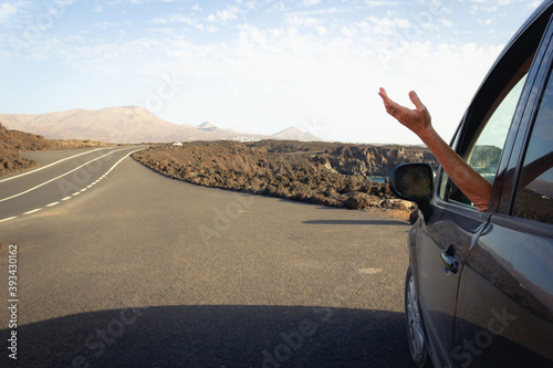 Arm of woman coming out of car window parked on side of road in Lanzarote volcanic island. Summer vacation, car rental, travel journey concepts