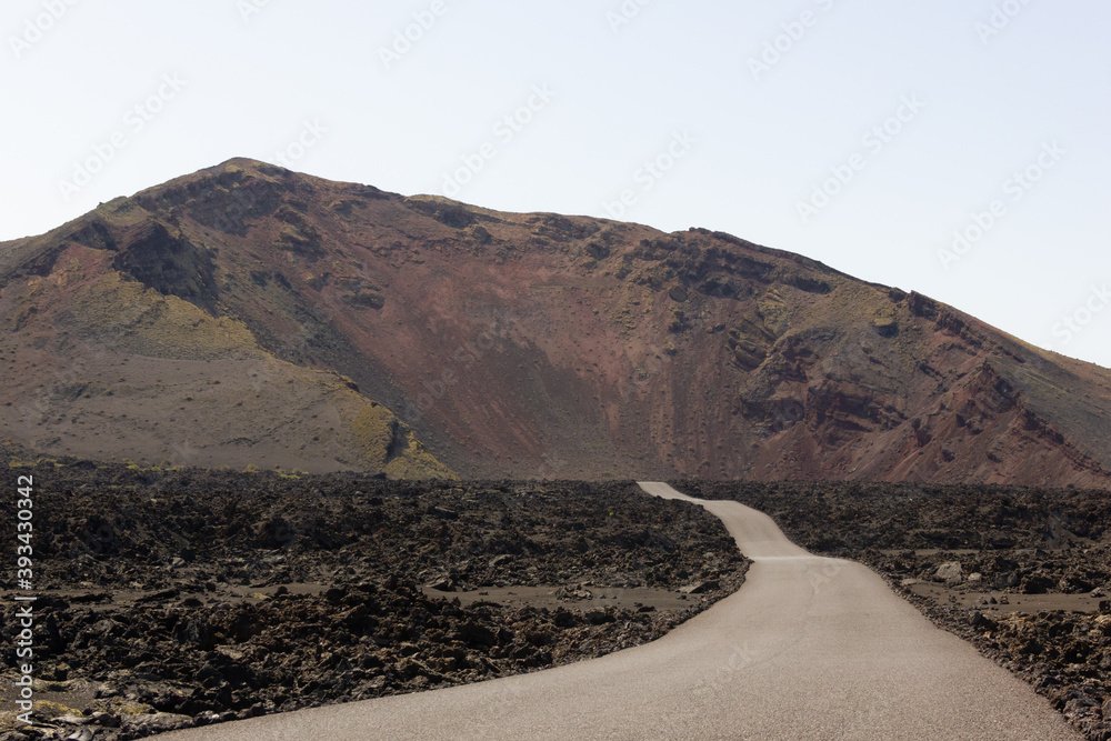 Empty road leading to volcano in Timanfaya National Park. Magnificent volcanic natural landscape in Lanzarote island. Travel destination, tourism attraction concepts