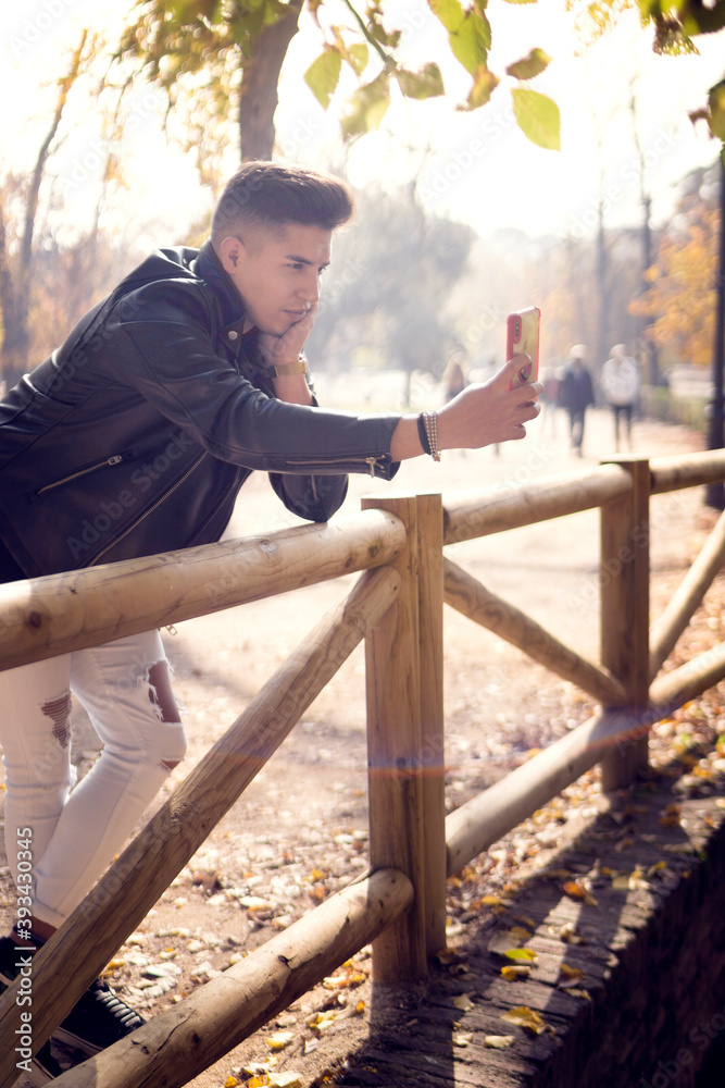 Young man in his 20s sitting on a bench taking selfie in the park Young man in his 20s sitting on a bench taking selfie in the park