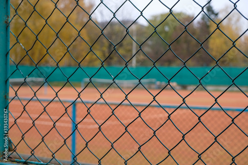 Wire mesh fence and blurred tennis court on an autumn day.