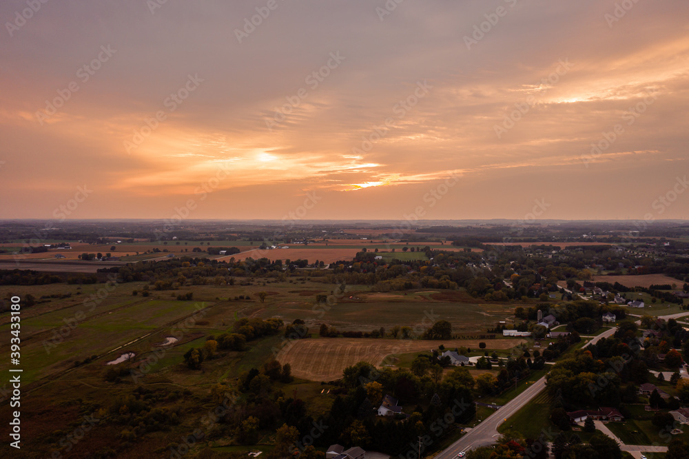 A beautiful aerial sunset sky and landscape photograph of a pink and orange colored clouds over rural farm land and homes near Slinger, Wisconsin.