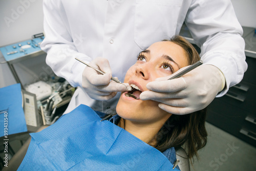 Male dentist in gloves examining oral cavity of pretty female patient at clinic