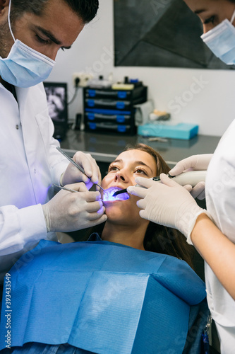 Male dentist examining teeth of female patient with help of assistant at clinic photo