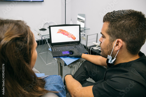 Male doctor showing picture of gums to female patient on laptop screen in clinic photo