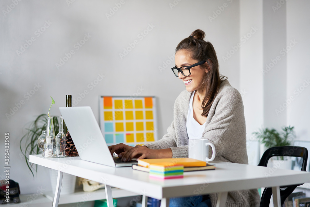 © Bartek Szewczyk/Westend61 - Smiling young woman at home using laptop on desk