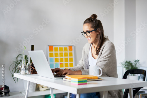 Smiling young woman at home using laptop on desk photo