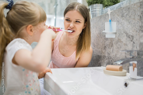 Mother and daughter brushing teeth in bathroom photo