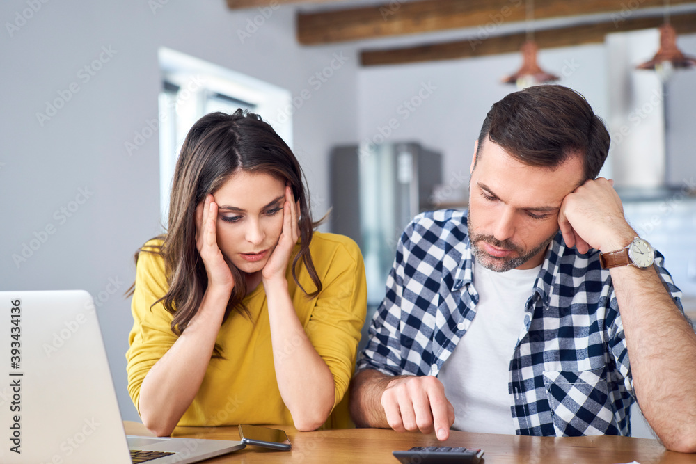 Worried couple sitting at dining table, using laptop, checking finances Worried couple sitting at dining table, using laptop, checking finances