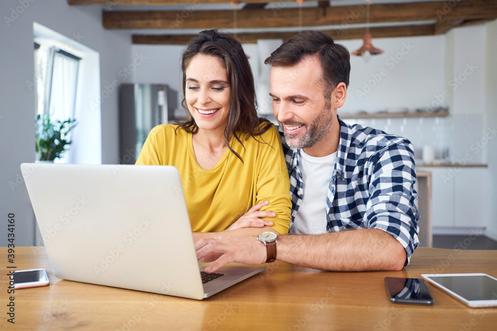 Couple sitting at dining table, using laptop, smiling Couple sitting at dining table, using laptop, smiling