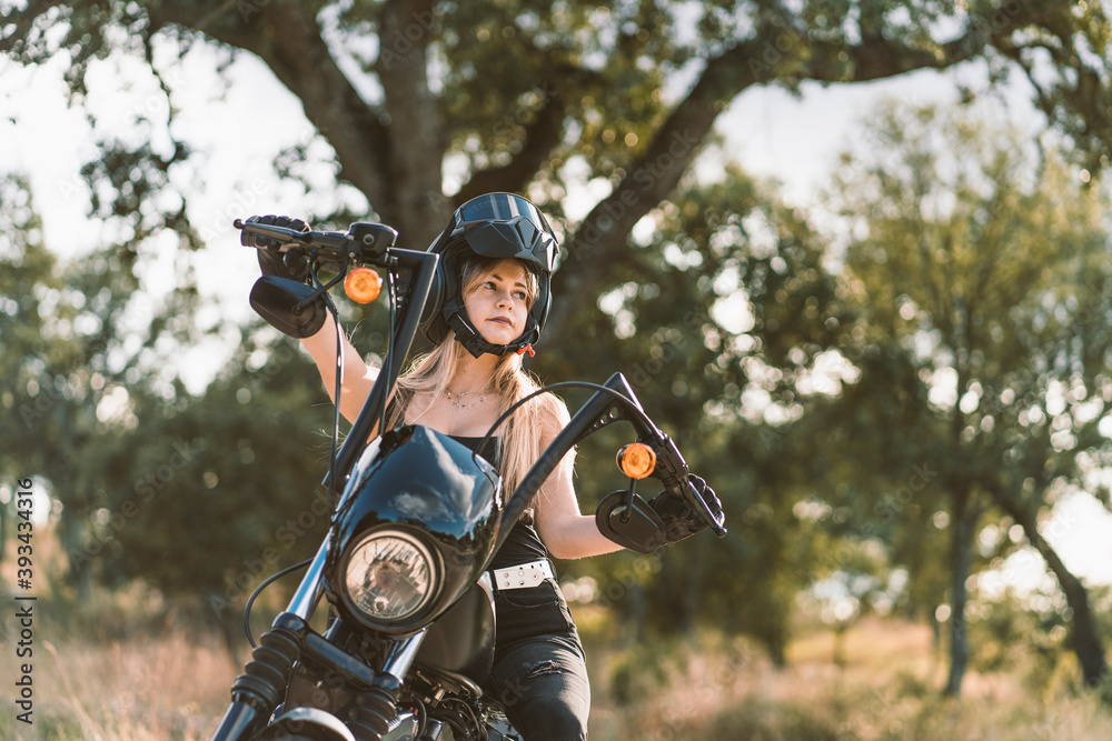 Beautiful woman wearing crash helmet while sitting on motorcycle against tree Beautiful woman wearing crash helmet while sitting on motorcycle against tree