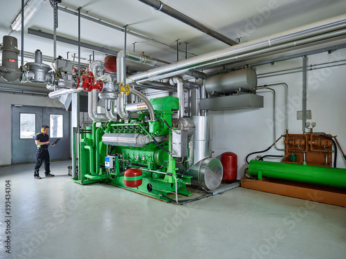 Combined heat and power plant, worker with ear defenders using laptop in front of gas engine