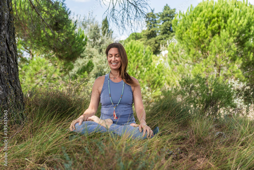 Smiling woman practicing yoga while sitting under tree on grass Smiling woman practicing yoga while sitting under tree on grass