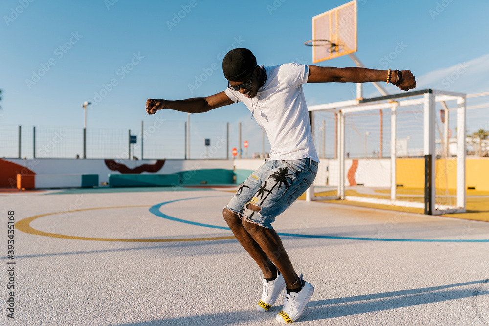 Carefree young man dancing in sports court against clear sky