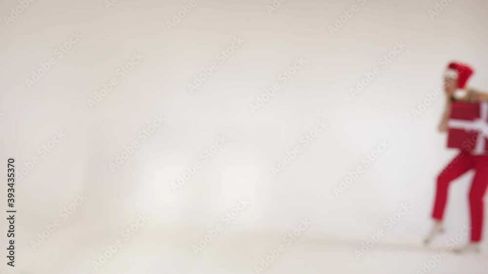 Full length of funny young woman in Santa hat walking while sneaking with a gift box for surprise, isolated on white background Full length of funny young woman in Santa hat walking while sneaking with a gift box for surprise, isolated on white background