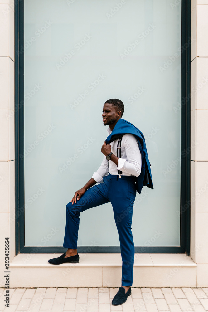 Smiling young male entrepreneur holding suit while standing by window in city Smiling young male entrepreneur holding suit while standing by window in city