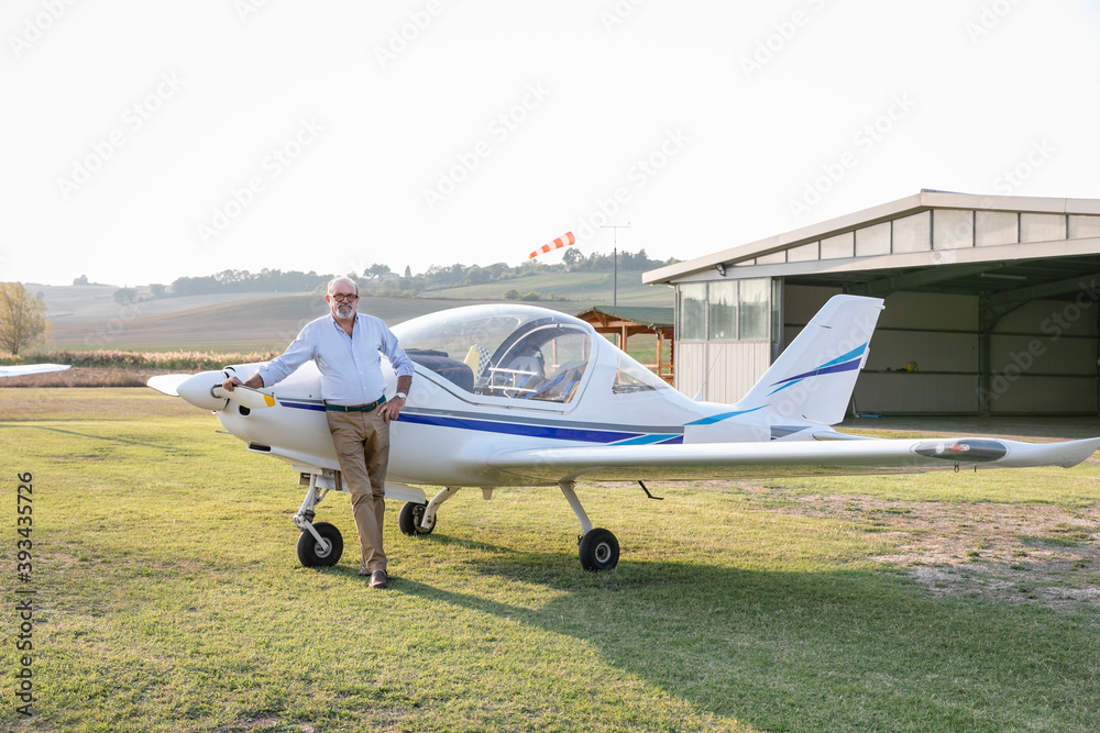 Senior man with hand on hip standing against airplane at airfield Senior man with hand on hip standing against airplane at airfield