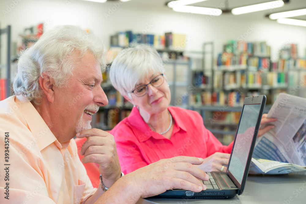 Senior couple with laptop and newspaper in a city library Senior couple with laptop and newspaper in a city library