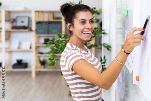 Happy female architect looking while pointing at whiteboard with felt tip pen at creative workplace photo