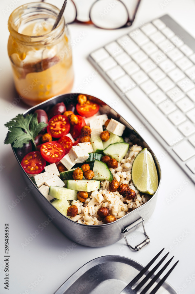 Lunch box with fresh vegan salad lying on desk in front of computer