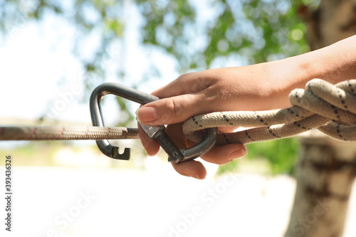 Woman using screw lock carabiner during training outdoors, closeup photo