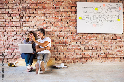 Businessman and woman sitting in a loft, giving high five, founding a start-up company