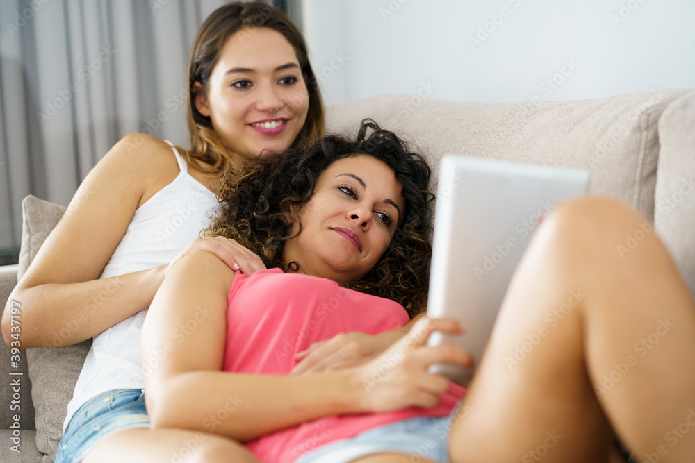 Beautiful lesbian couple using digital tablet while lying on sofa at home Beautiful lesbian couple using digital tablet while lying on sofa at home