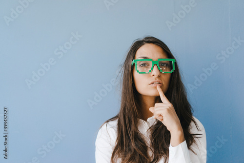 Young woman wearing pixel glasses, putting finger on mouth photo