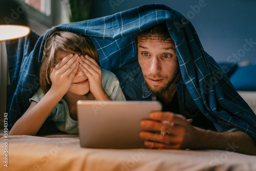 Excited father and son watching a movie on tablet under blanket photo