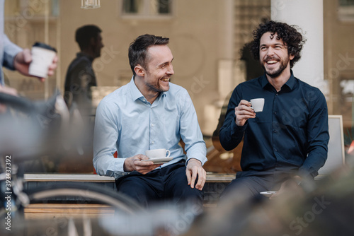 Friends sitting in front of coffee shop, talking, drinking coffee