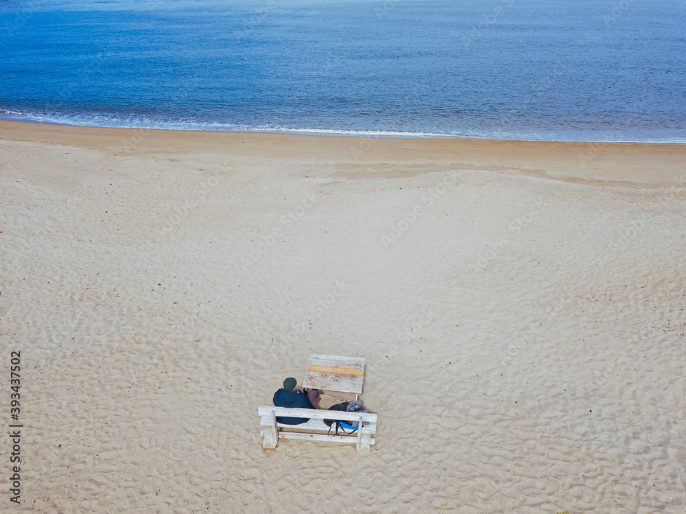 Aerial view of man sitting on bench at beach Aerial view of man sitting on bench at beach