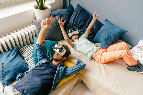 Father and son wearing VR glasses lying down at home photo