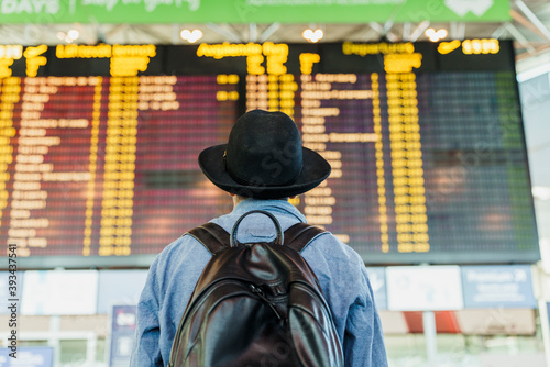 Young man with hat and backpack looking at arrival departure board at the airport photo