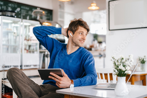 Smiling man in a cafe with earphone, laptop and tablet photo